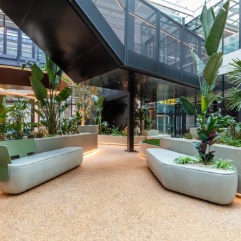 Yarra Falls, Melbourne, featuring a premium biophilic atrium with lush tropical planting, integrated sculptural seating, contemporary architectural bridges, floor-to-ceiling glazing, and abundant natural light, creating a wellness-focused workplace environment that supports collaboration, tenant wellbeing, and connection to nature within a landmark commercial campus.