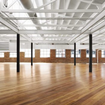 Yarra Falls, Melbourne, featuring a premium warehouse-style office floor with expansive open-plan accommodation, polished timber flooring, exposed heritage brick walls, white-painted steel trusses, high sawtooth ceilings, and abundant natural light. The space showcases the property's industrial heritage character while providing flexible workplace accommodation suited to contemporary office, creative, and collaborative work environments.