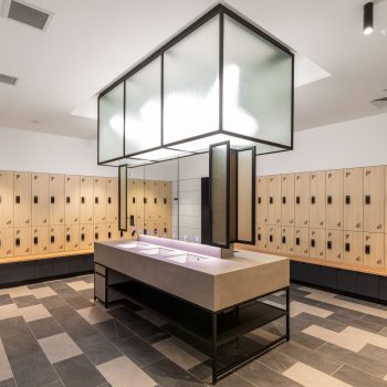 Industry Lanes, Melbourne, featuring premium end-of-trip facilities with secure digital lockers, integrated timber bench seating, a central communal vanity and grooming station, textured glass architectural lighting, and contemporary wellness-focused design that supports active commuting, employee wellbeing, and an elevated workplace experience.