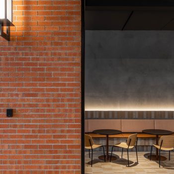 Industry Lanes, Melbourne, featuring a premium workplace collaboration lounge with exposed red-brick walls, upholstered banquette seating, contemporary timber chairs, café-style tables, and industrial-inspired architectural detailing that supports informal meetings, workplace connection, and tenant wellbeing within a heritage-led commercial precinct.