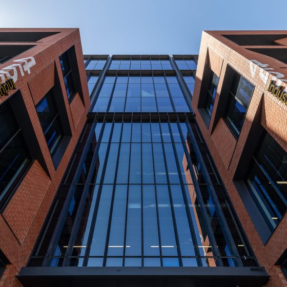 Industry Lanes, Melbourne, featuring a striking commercial office façade with bold red-brick architecture, expansive floor-to-ceiling glazing, deep recessed window openings, and prominent Industry Lanes branding, creating a distinctive workplace destination that celebrates industrial heritage while delivering contemporary premium office accommodation.